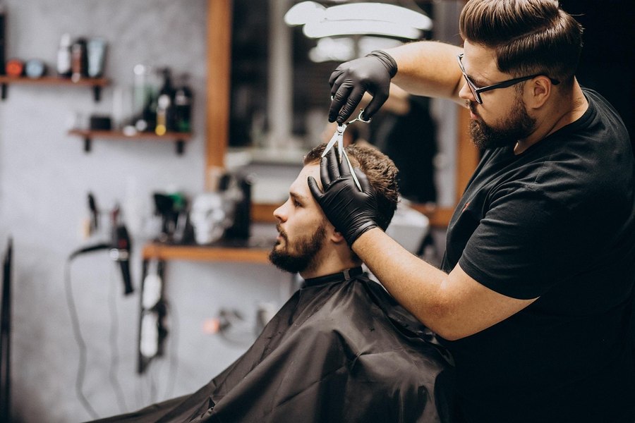 Barbero con guantes negros cortando el cabello a máquina (imagen de referencia)